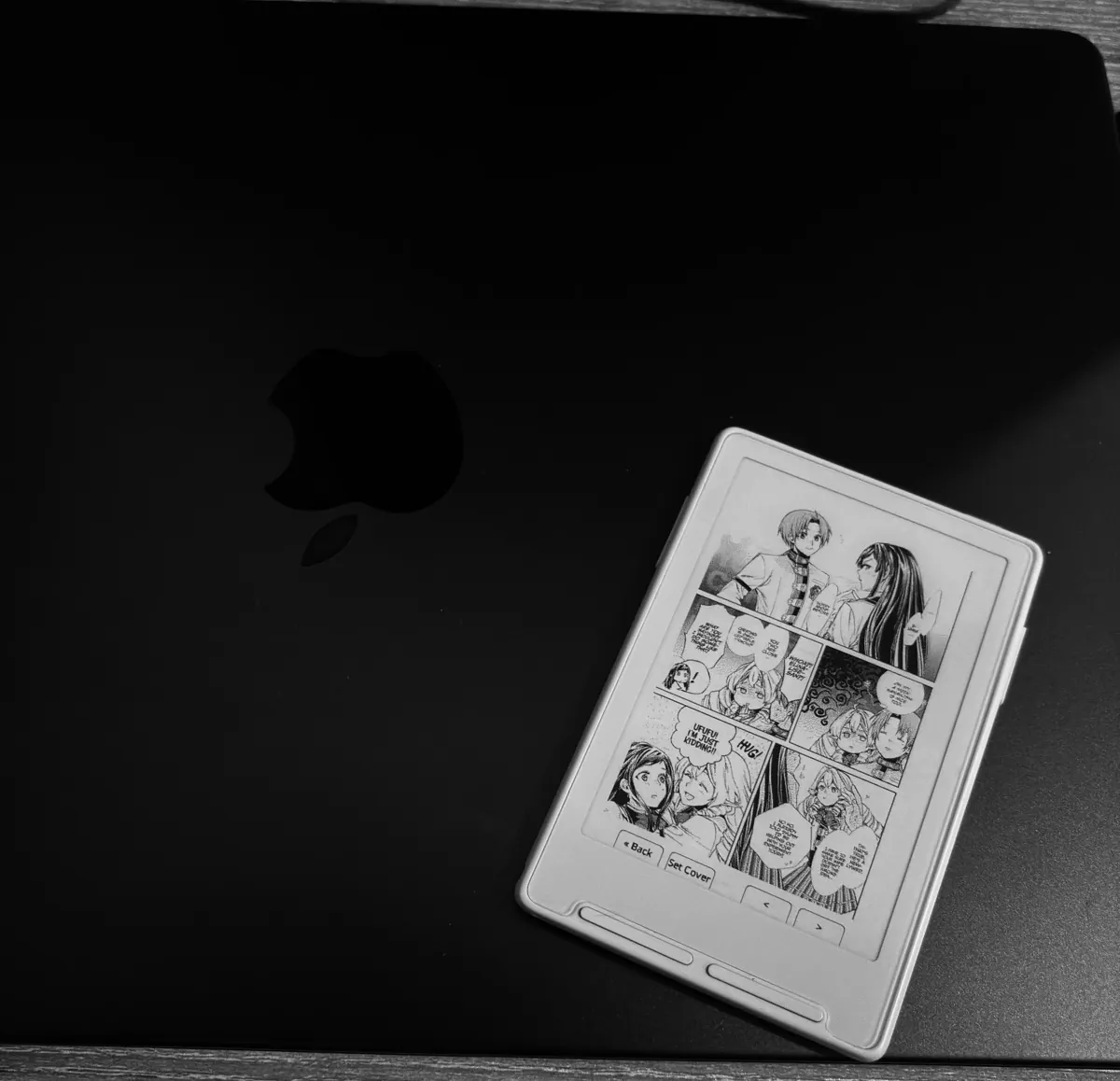 A manga page printed on the Xteink X3, resting on a closed MacBook.